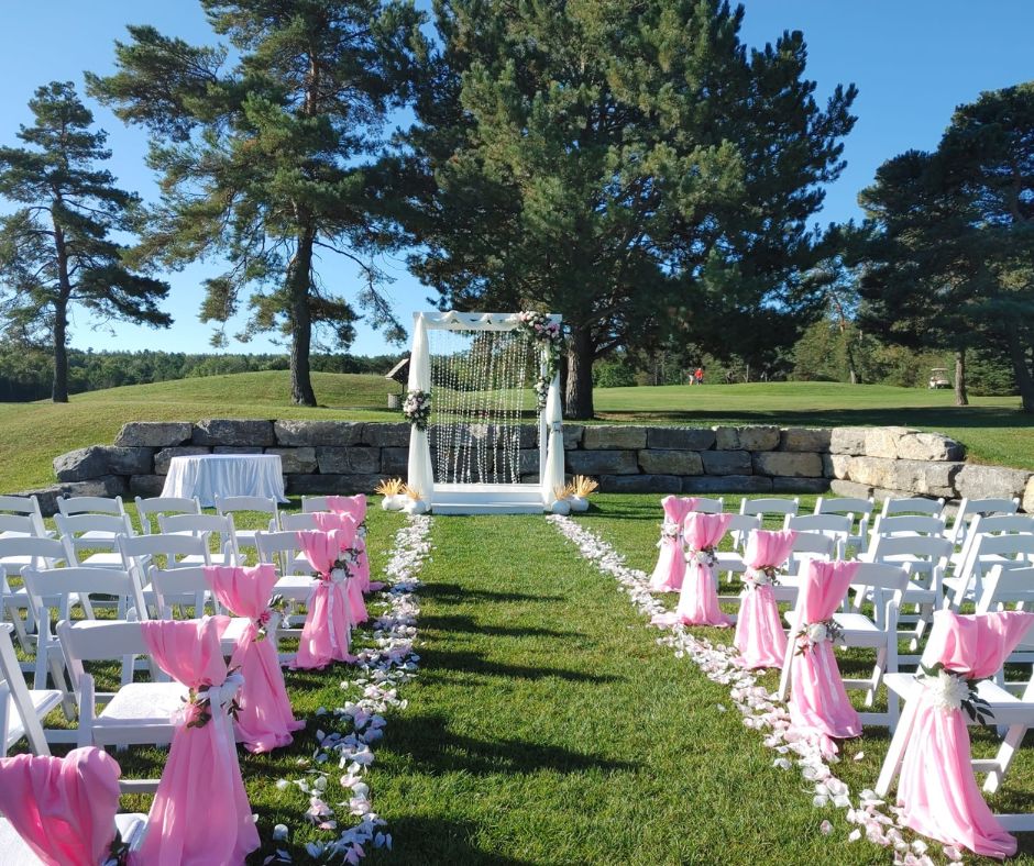 Image of the Clubhouse garden set up with white chairs and pink drapery with an altar at the front and flower petals outlining the aisle for a wedding